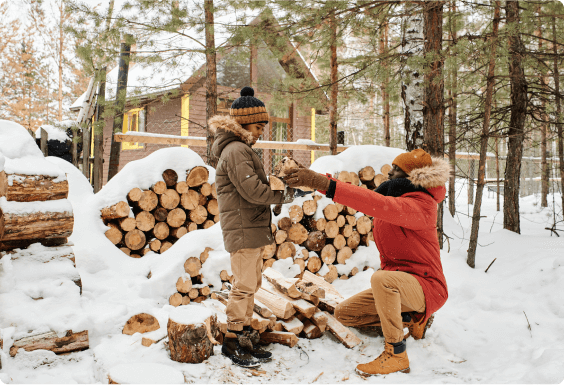 Father and son gathering up pre-chopped firewood at a large wood pile 